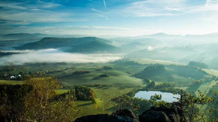 Krajina českého pohraničí za svítání — mlha nad údolím, lesy a rybník